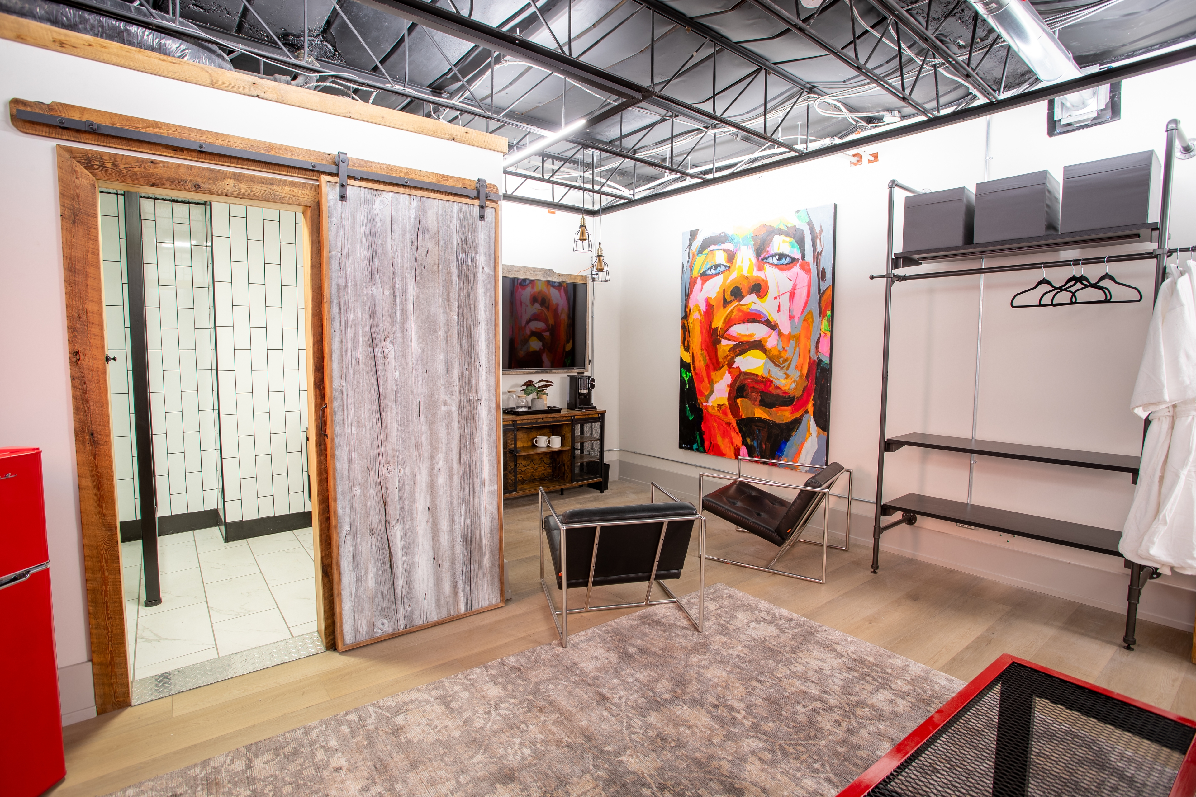 A vibrant industrial-loft room with a rustic sliding barn door, bold abstract art, modern furniture, and a black exposed ceiling.