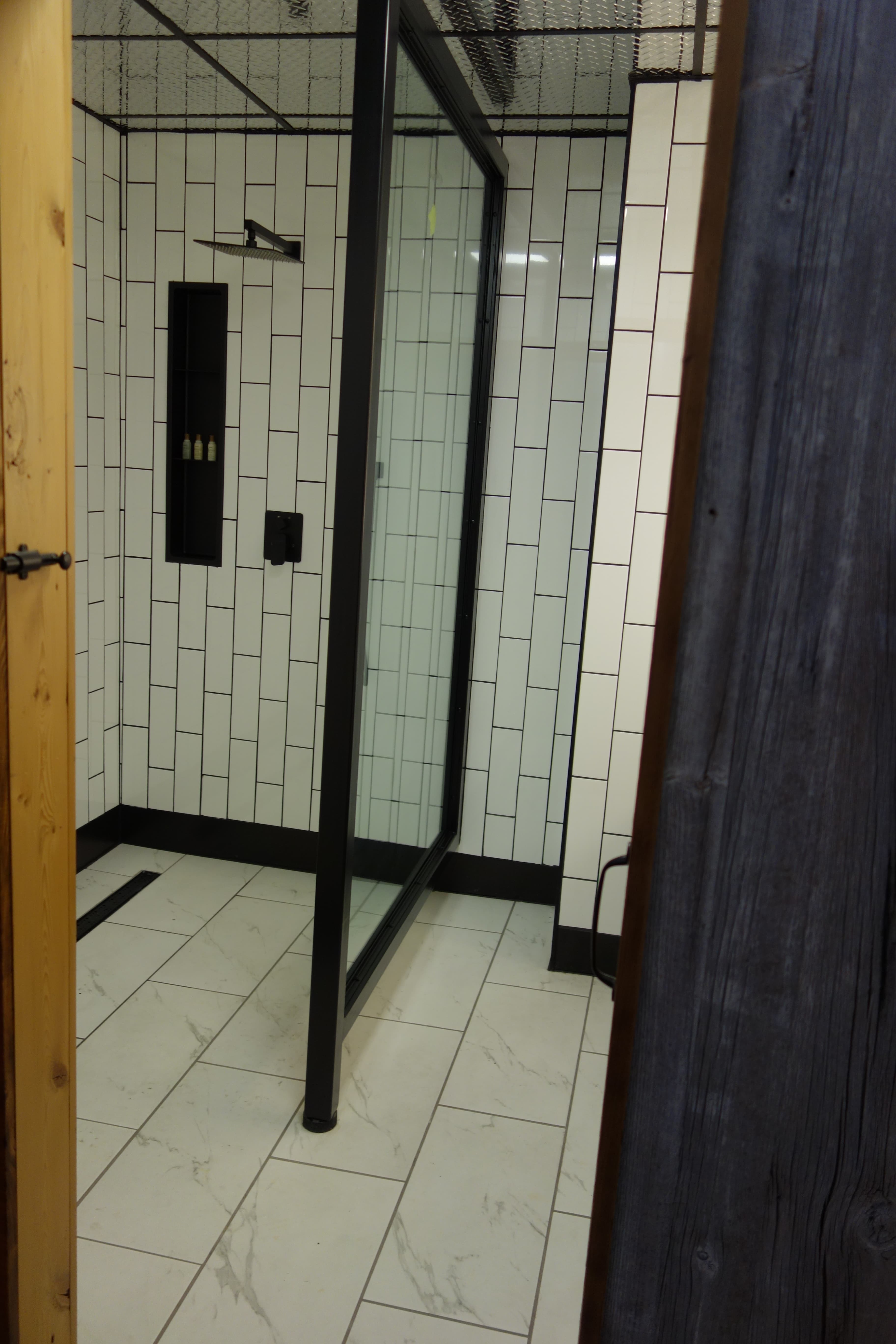 A stylish, modern bathroom featuring a large walk-in shower with a black metal frame, white vertical subway tiles, and black fixtures.