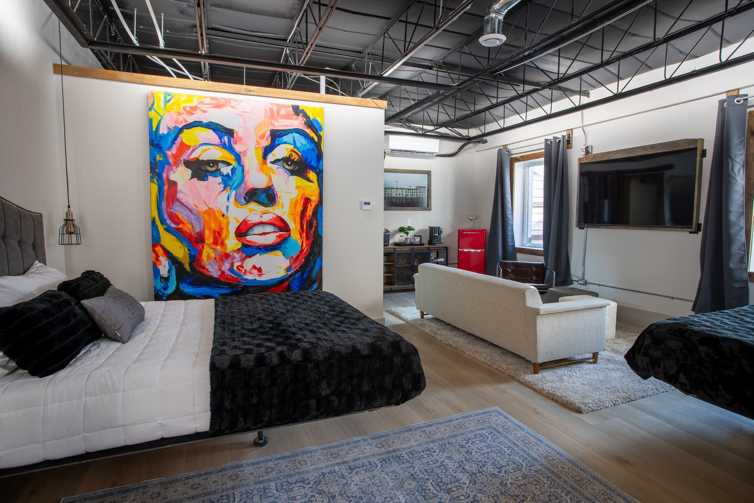 A vibrant, spacious hotel suite with two queen beds, a white sofa, and a large pop art mural of Marilyn Monroe on the wall.