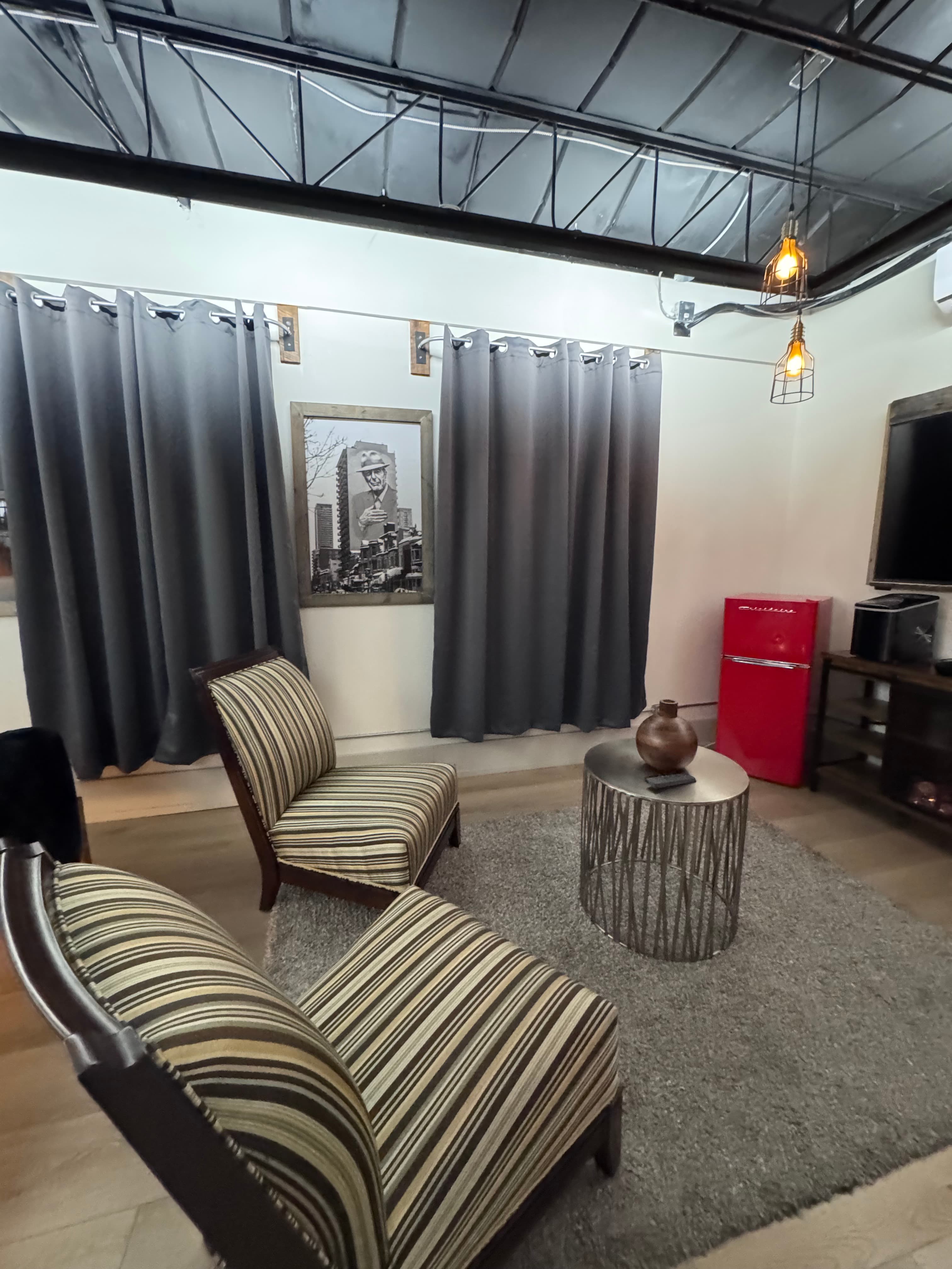 A cozy living room featuring two striped chairs, a circular coffee table, a gray rug, and a red refrigerator.