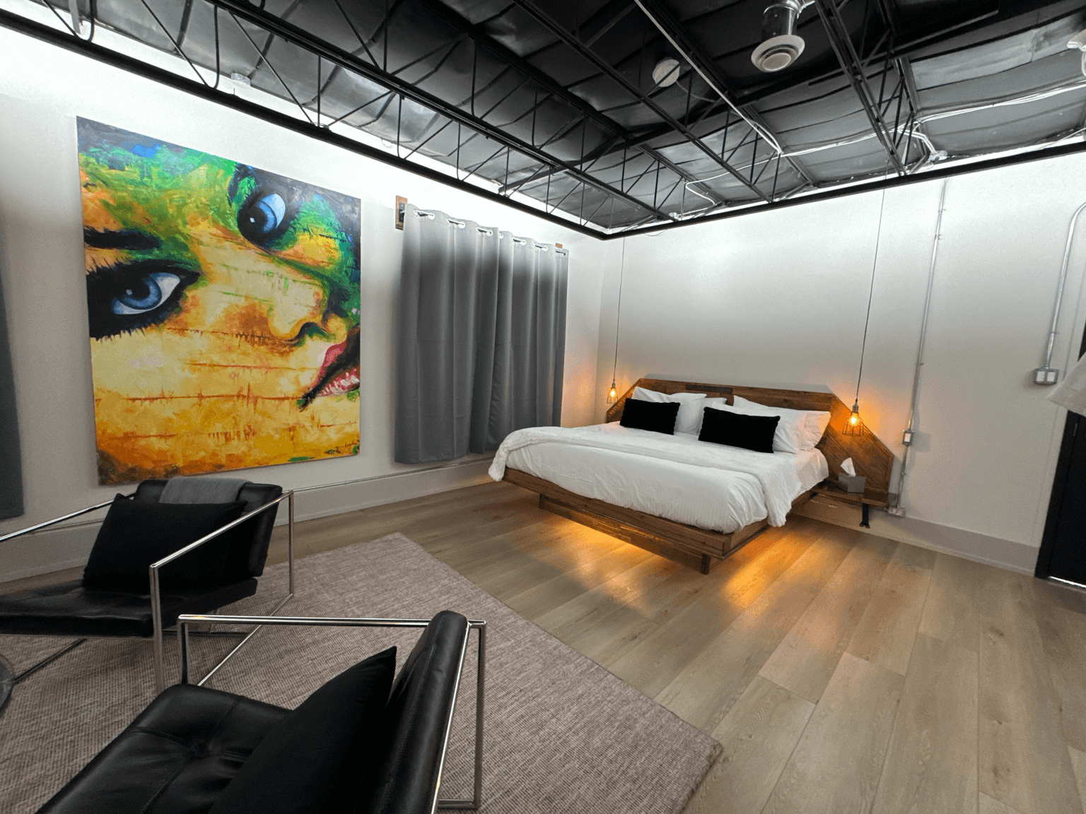 A modern bedroom featuring a large colorful artwork, a wooden bed, and sleek furniture.