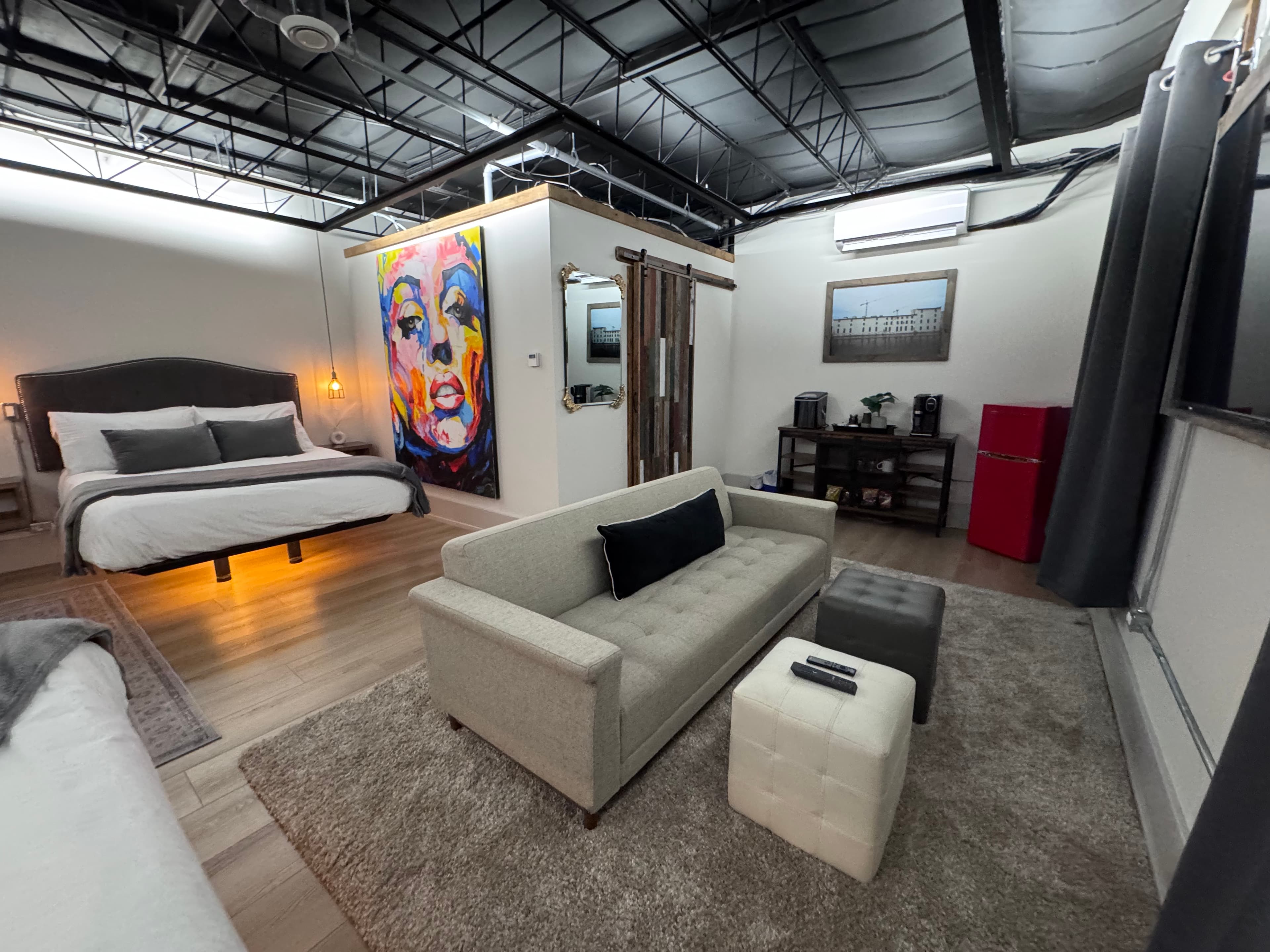 A modern bedroom and lounge area featuring a large bed, colorful wall art, a sofa, and a small table.