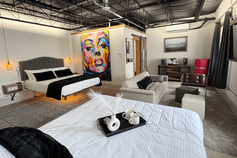 A stylish hotel room featuring a bed, an abstract portrait, and modern furniture.