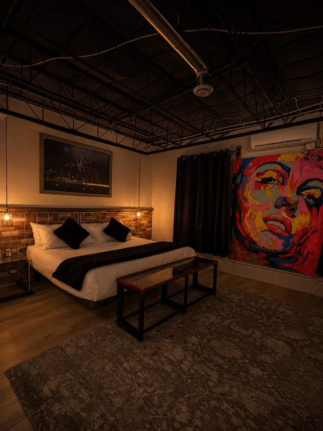 A cozy bedroom featuring a bed with black and white bedding, a colorful mural of a face, and warm pendant lighting.