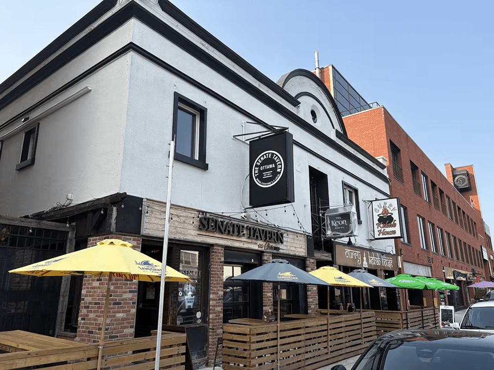 A street view of the Senate Tavern, featuring yellow and green umbrellas on an outdoor patio.