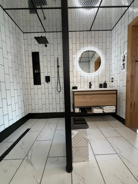 Modern bathroom with white tile walls, a circular mirror, and a wooden vanity.