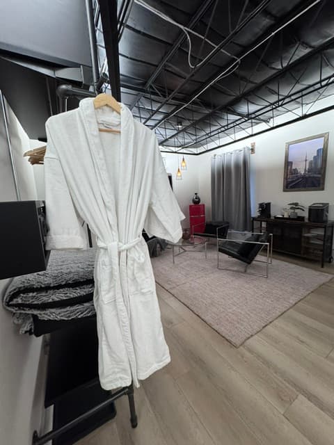 A white bathrobe hangs on a rack in a modern living room with a rug and minimal furniture.