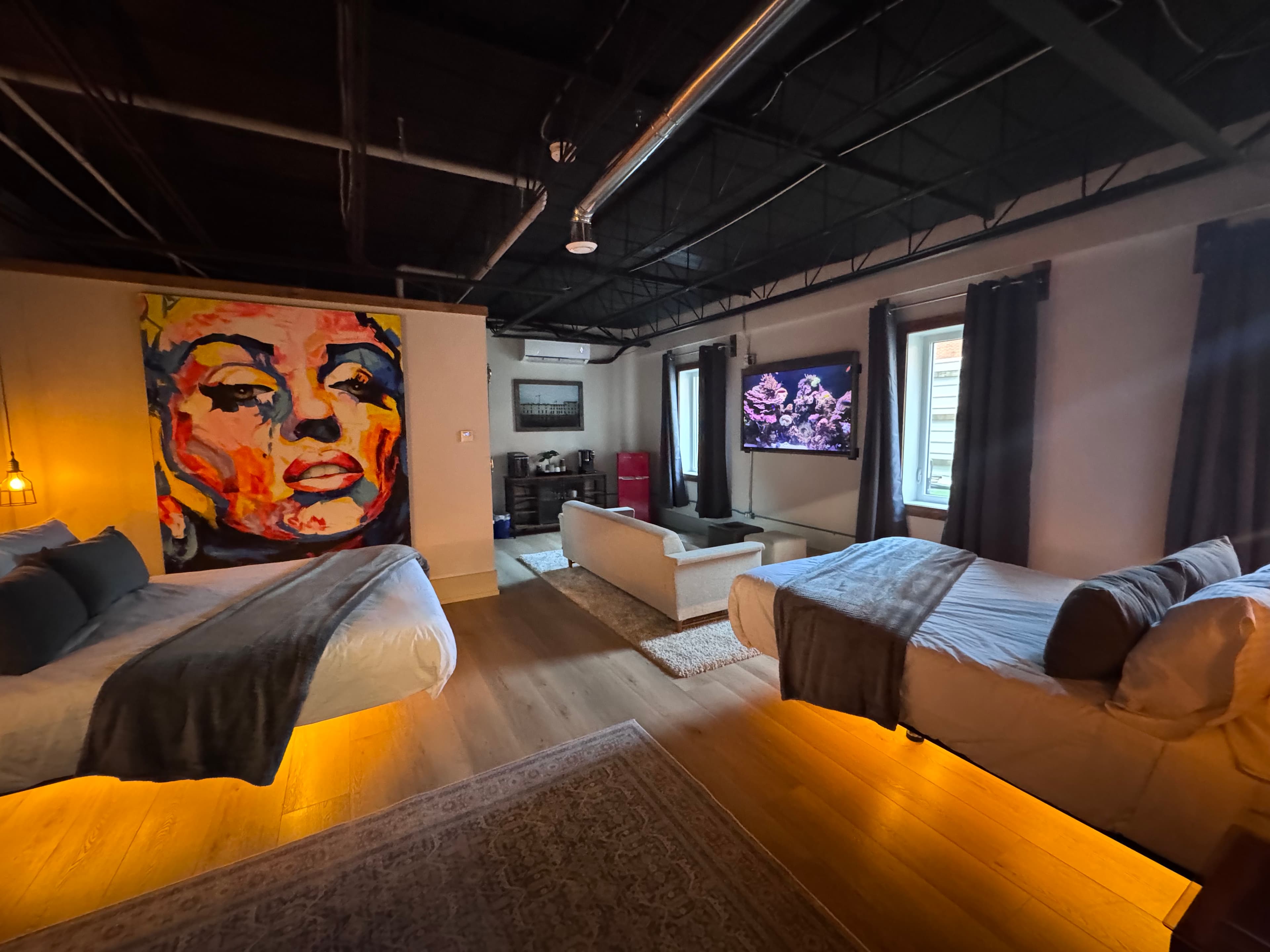 A stylish bedroom with two beds, modern decor, and a vibrant wall art of a woman's face.