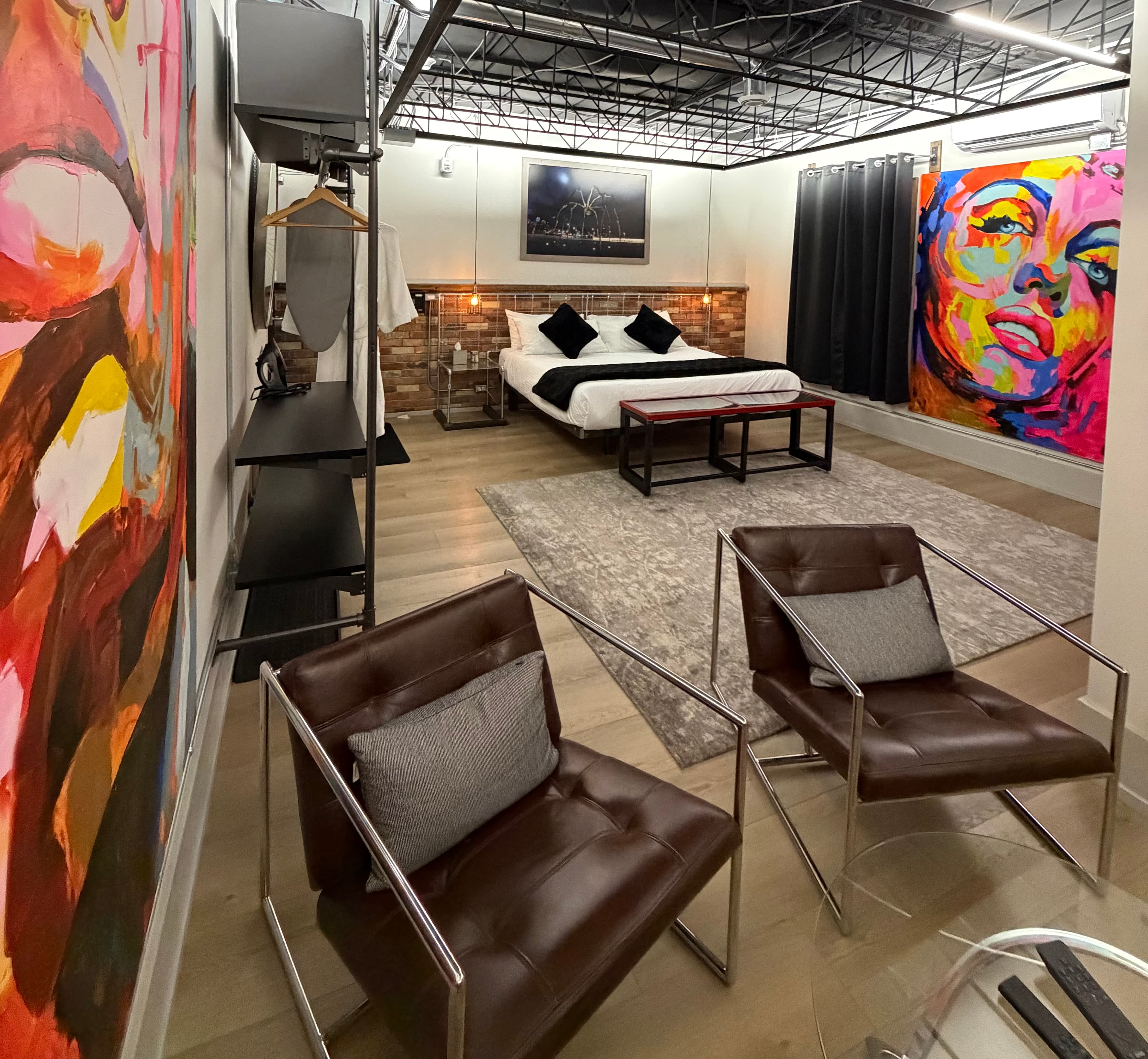 A contemporary bedroom with a bed, two chairs, colorful artwork, and modern decor.