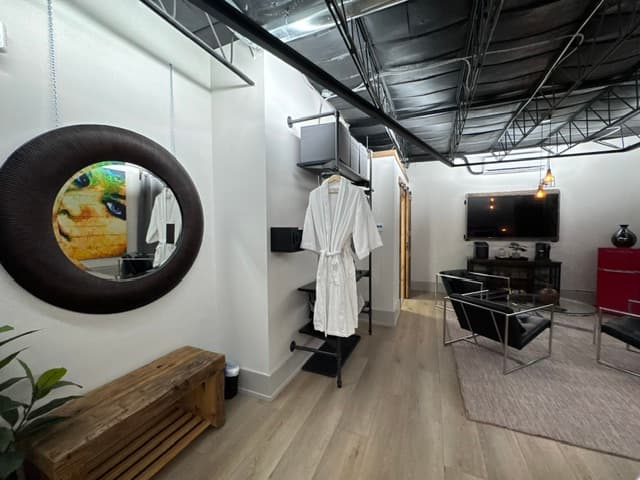 A modern, well-lit interior featuring a mirror, hanging robe, shelves, and seating area.