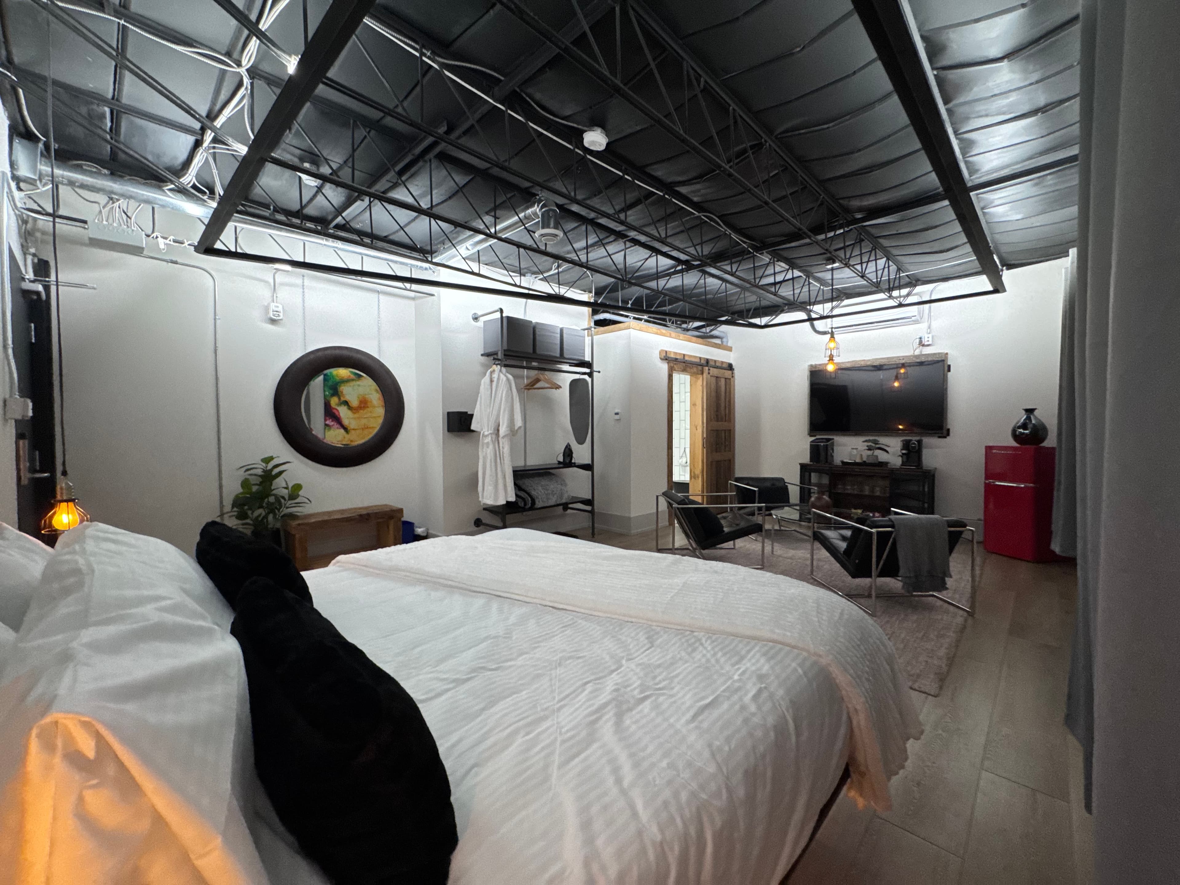 A modern, minimalistic bedroom featuring a large bed, seating area, wall-mounted TV, and stylish decor.