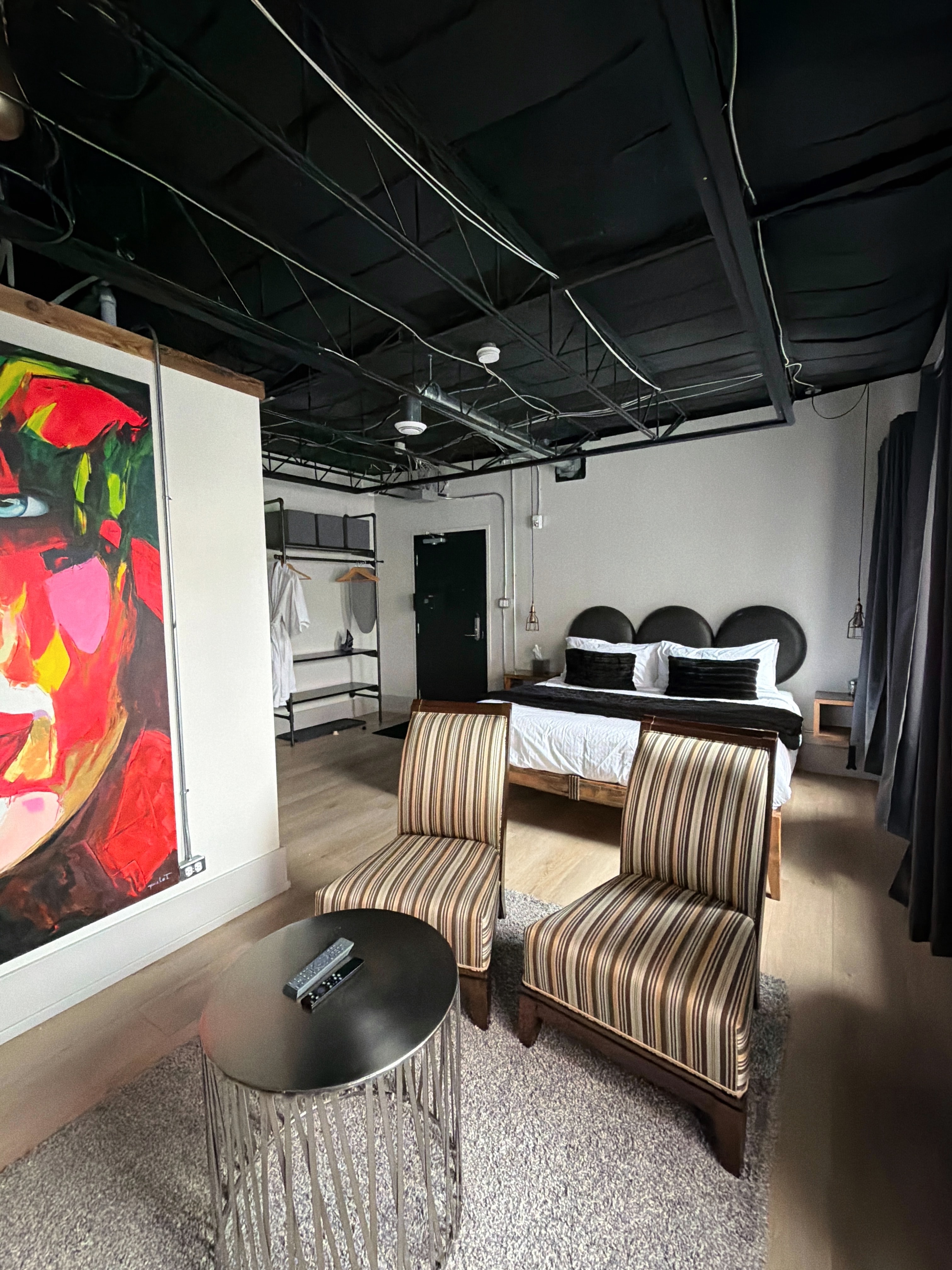 A modern hotel room featuring a painted wall, two striped chairs, a round table, and a bed with decorative pillows.