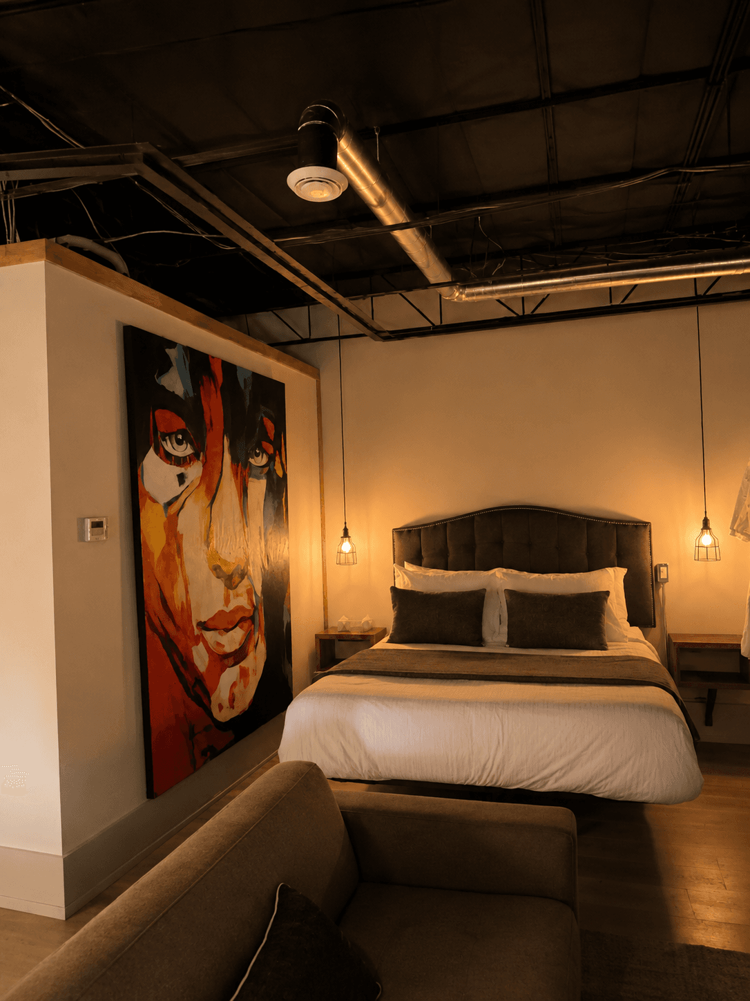A stylish bedroom featuring a large artwork of a face, a plush bed, and a modern seating area.