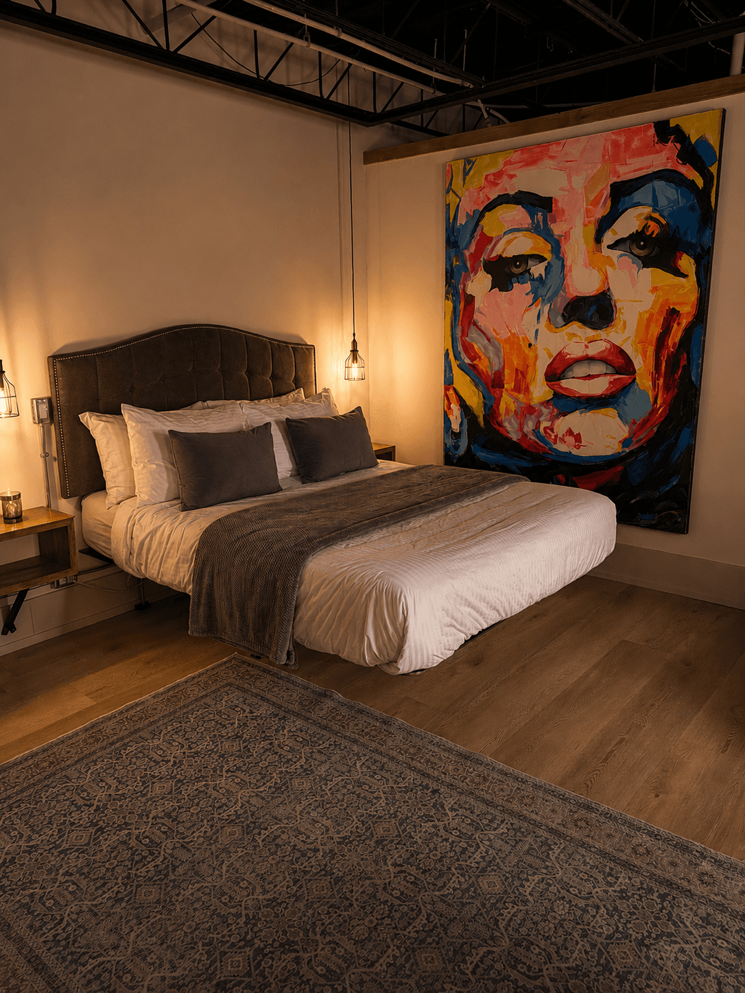 A stylish bedroom featuring a large bed, soft blankets, and a colorful portrait on the wall.